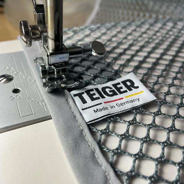 Das Tuch ist zu sehen wie es in einer Nähmaschine hergestellt wird. Es ist das Webetikett mit Made in Germany zu sehen